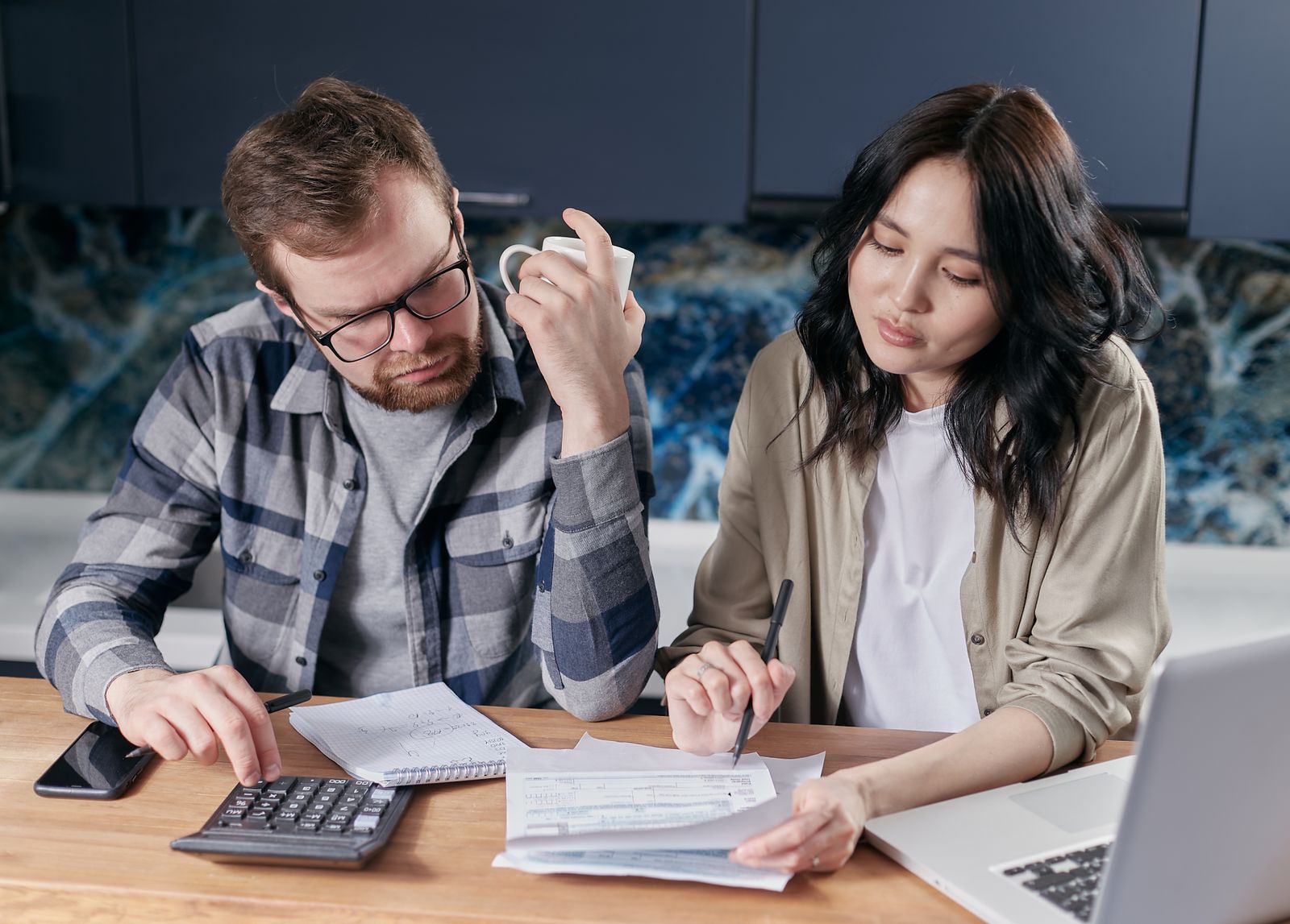 Un couple fait ses comptes avec une calculatrice à la table de la cuisine