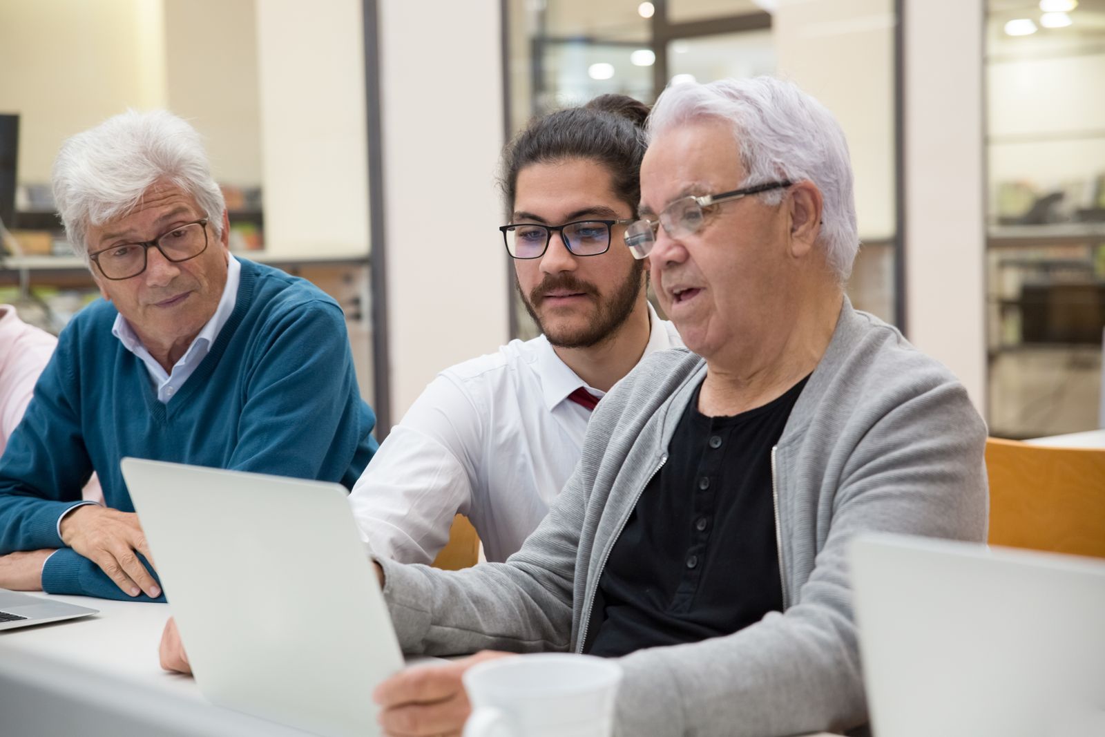 Un jeune homme aide deux seniors devant un ordinateur portable